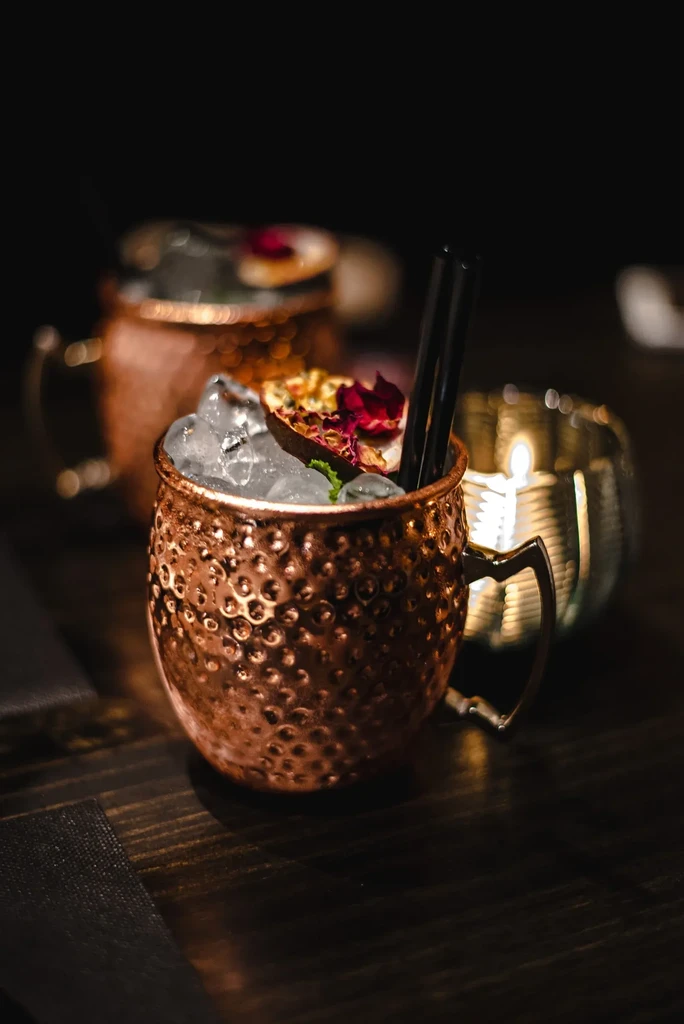 Close-up: Hammered copper mug cocktail with mint, citrus, and petals.