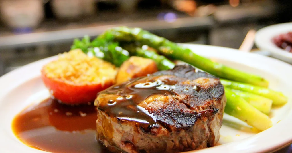 Grilled steak with dark sauce, stuffed tomato, and asparagus on a white plate.