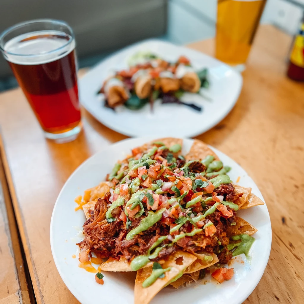 Eye-level shot of loaded nachos, fried items, and beers on a table.