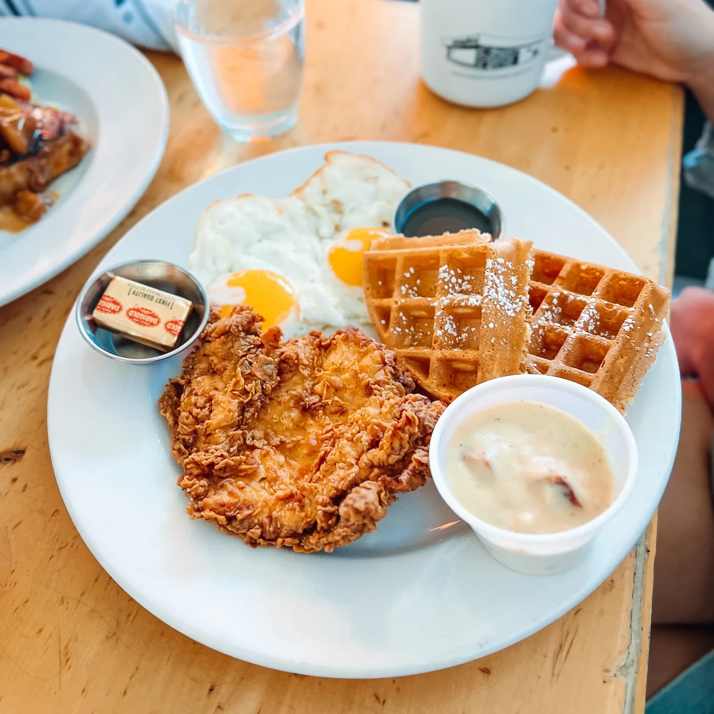 Fried chicken, waffles, eggs, toast, gravy, and syrup on a plate.