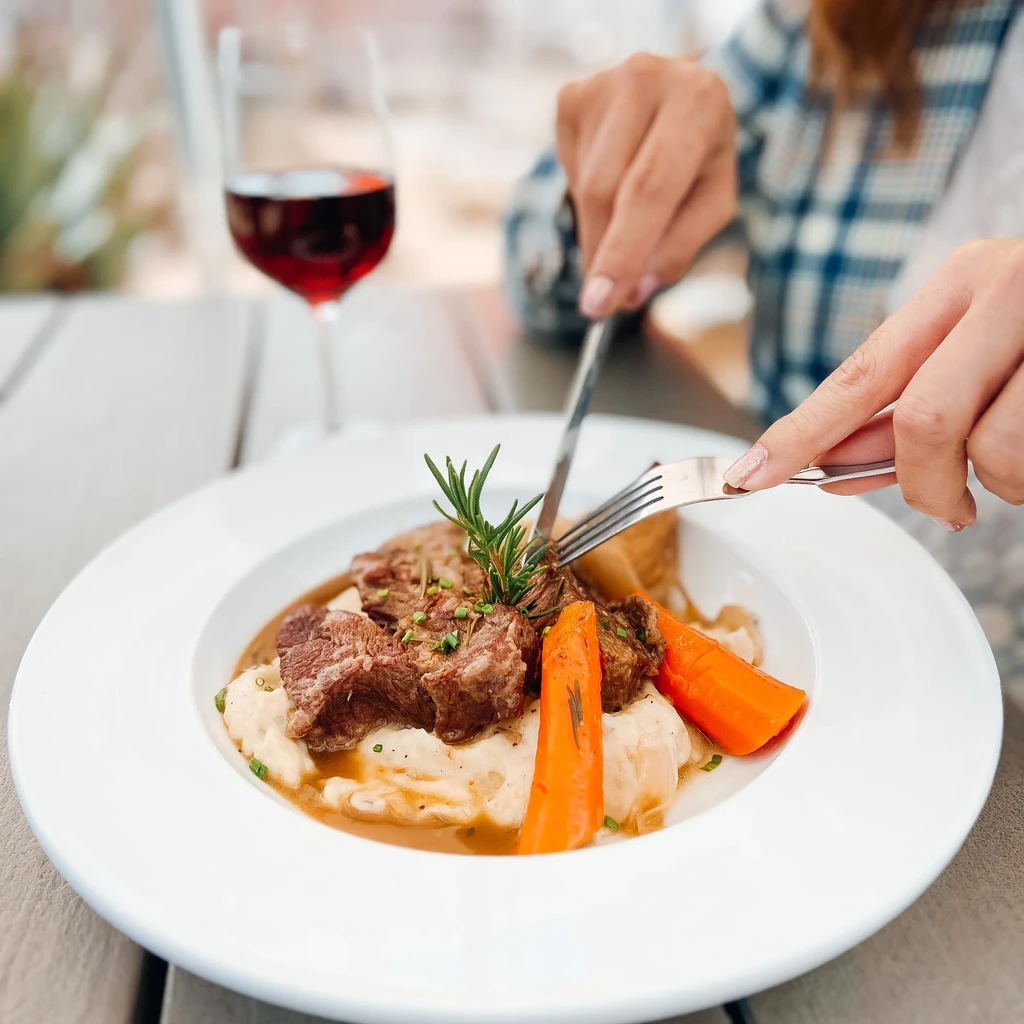 Hands cutting into braised beef, mashed potatoes, and carrots.