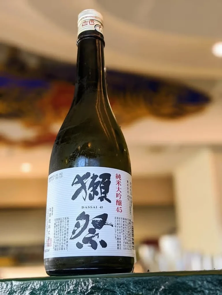 Dassai 45 sake bottle, chilled, with a blurred warm background.