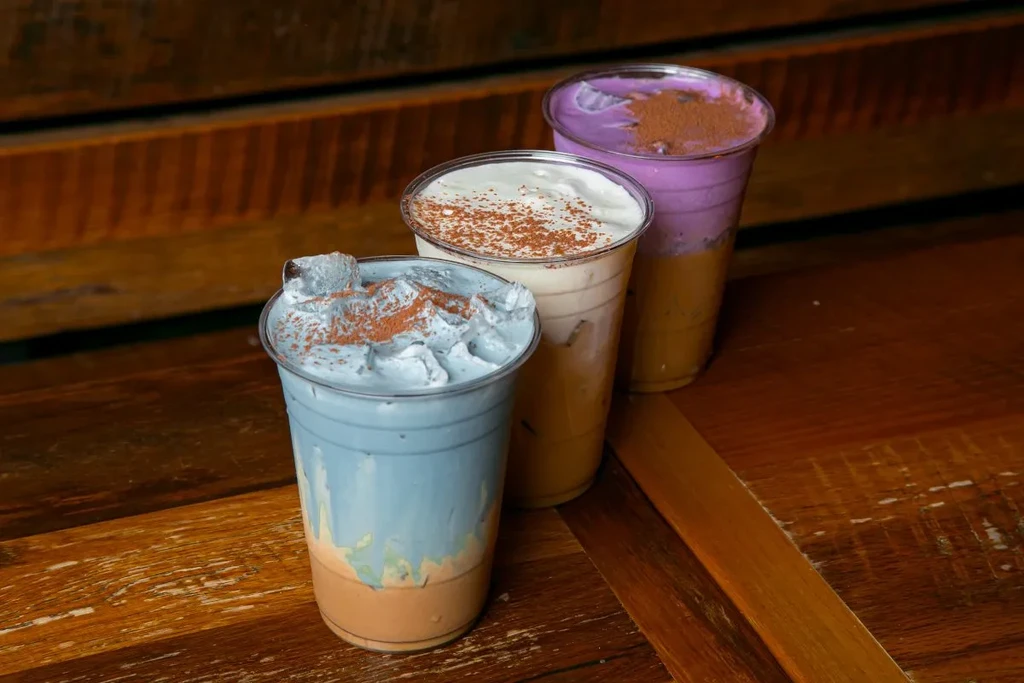 Three colorful layered iced drinks with whipped cream on wood.