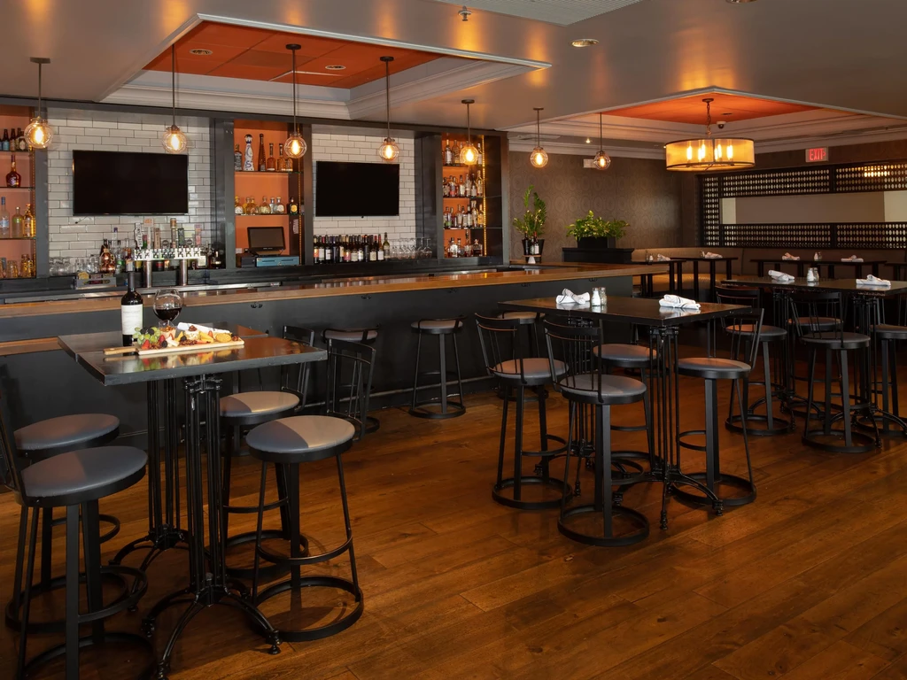 Upscale restaurant bar interior with high-top tables, wine, charcuterie.