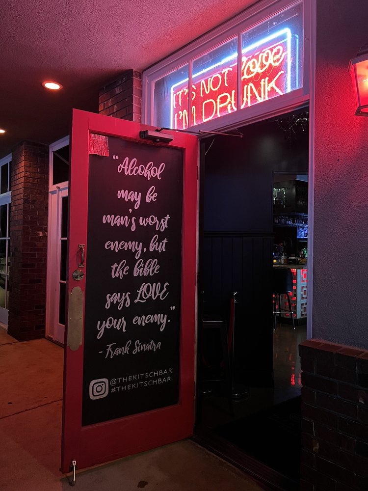 Red-lit bar entrance with chalkboard quote and neon sign.