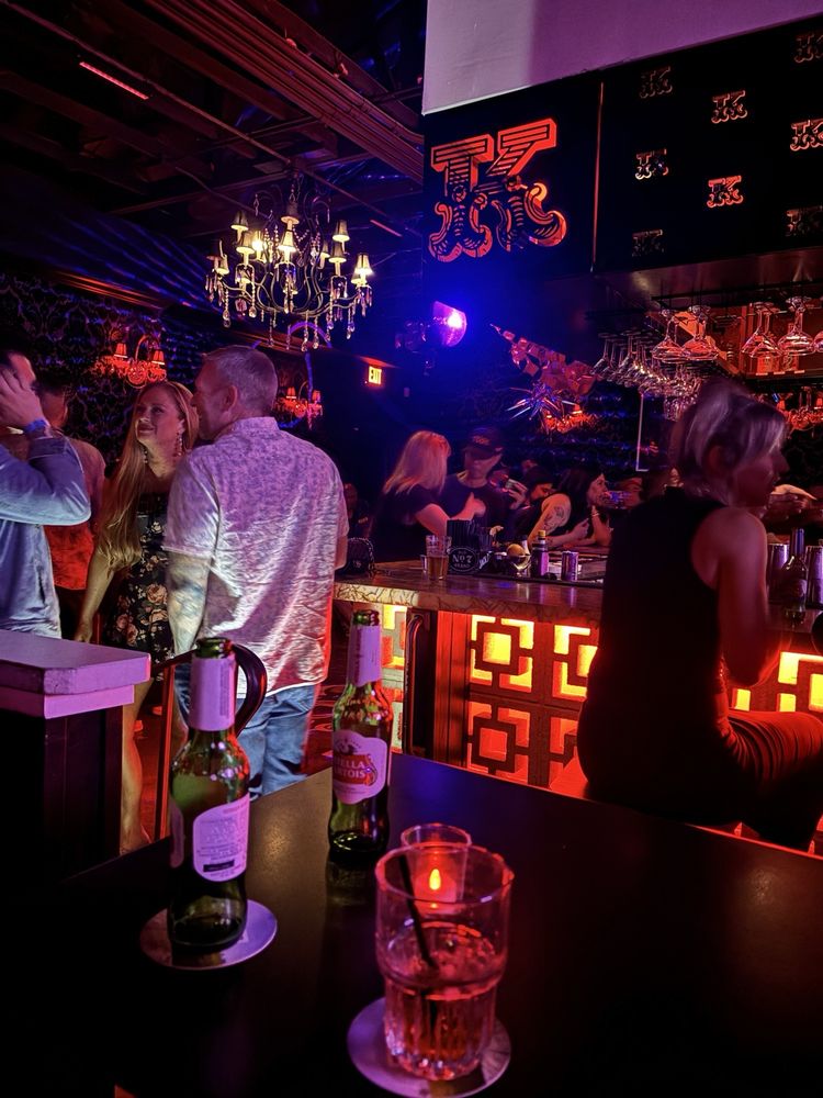 Patrons enjoying drinks at a dimly lit bar with red and blue lights.