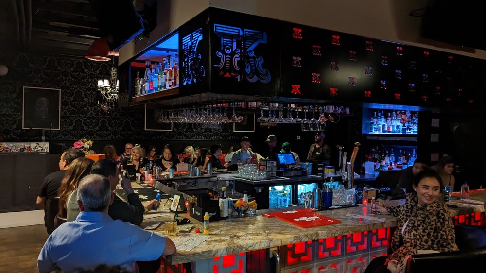Dark bar interior with patrons sitting at a marble counter.