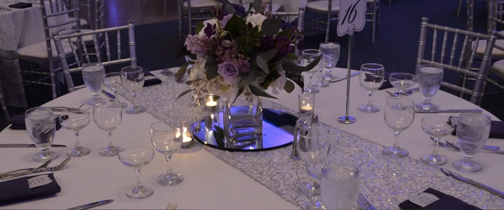 Elegantly set dining table with purple floral centerpiece, candles, and table number 16.