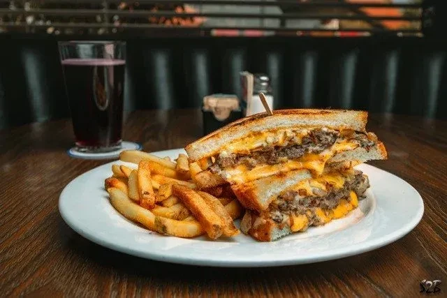 Close-up of a patty melt, golden fries, and drink on a restaurant table.