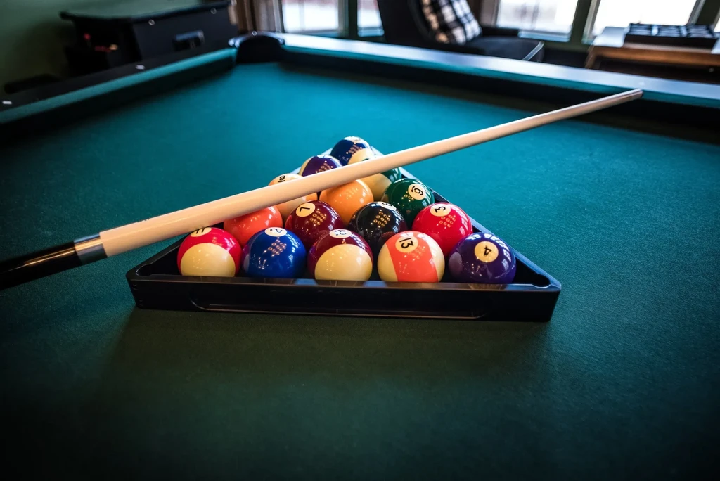 Colorful pool balls racked on green felt with a cue stick.
