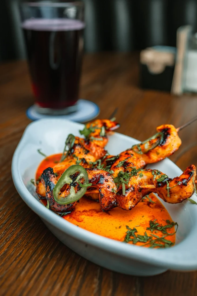 Grilled shrimp skewers with orange sauce, herbs, and a jalapeño.