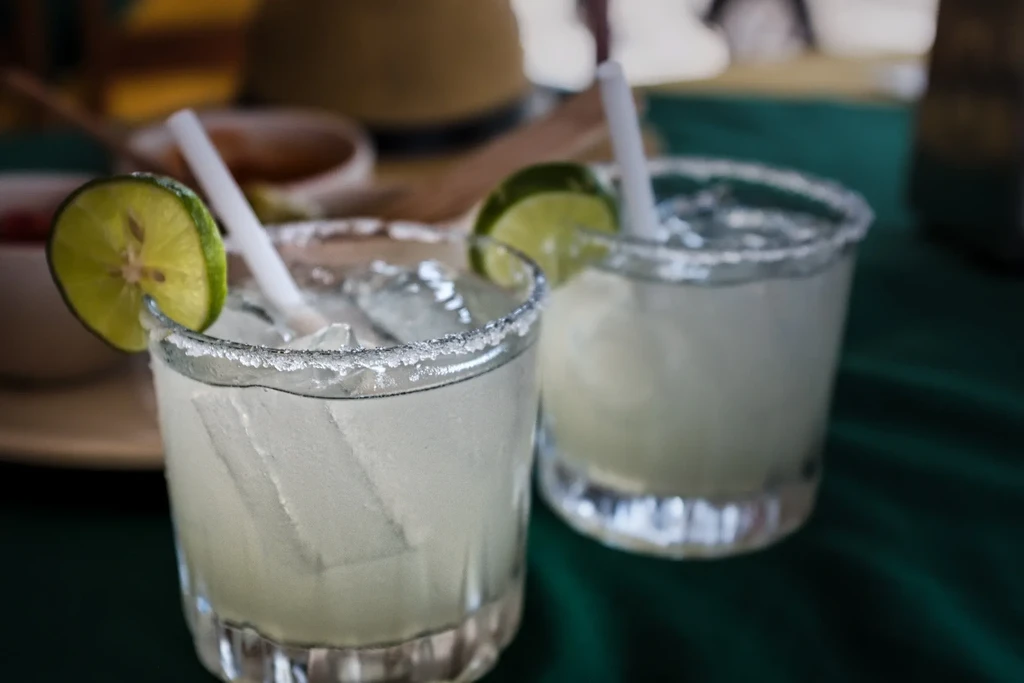 Two clear cocktails with salt rims, lime wedges, and ice.