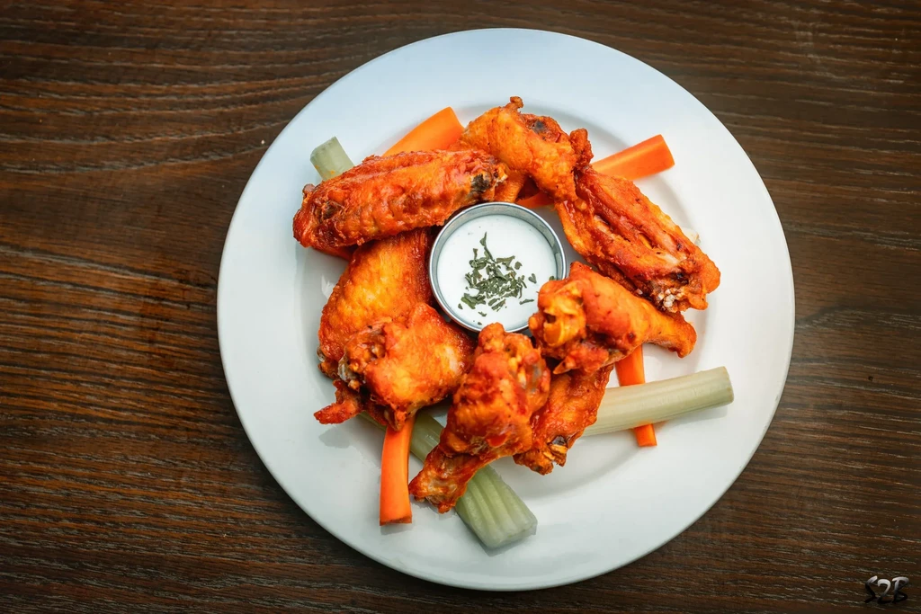 White plate of hot wings, creamy dip, carrot and celery sticks.