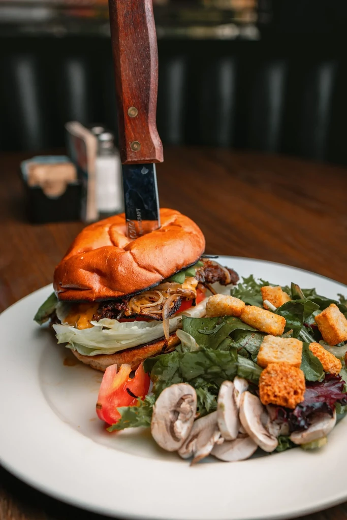 Gourmet burger impaled with a steak knife, served with side salad.