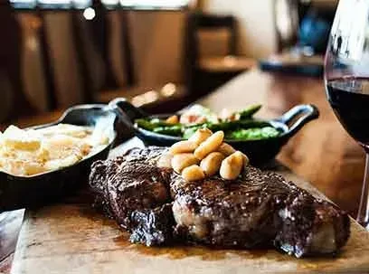 Well-cooked steak meal with creamy side, green vegetables, and red wine.