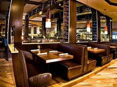 Empty upscale restaurant with dark leather booths, wooden tables, elegant lighting.
