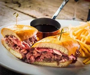 French dip sandwich with roast beef, au jus, and french fries.