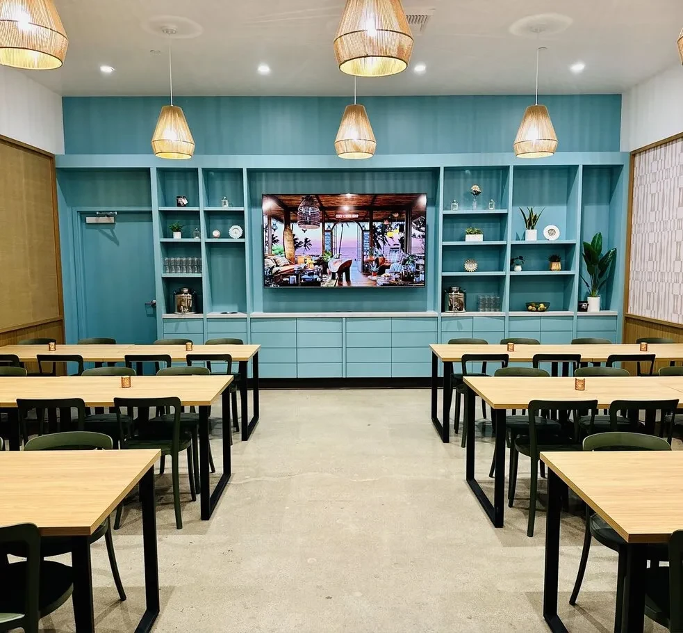 Modern dining space, teal walls, wooden tables, TV shows beach.