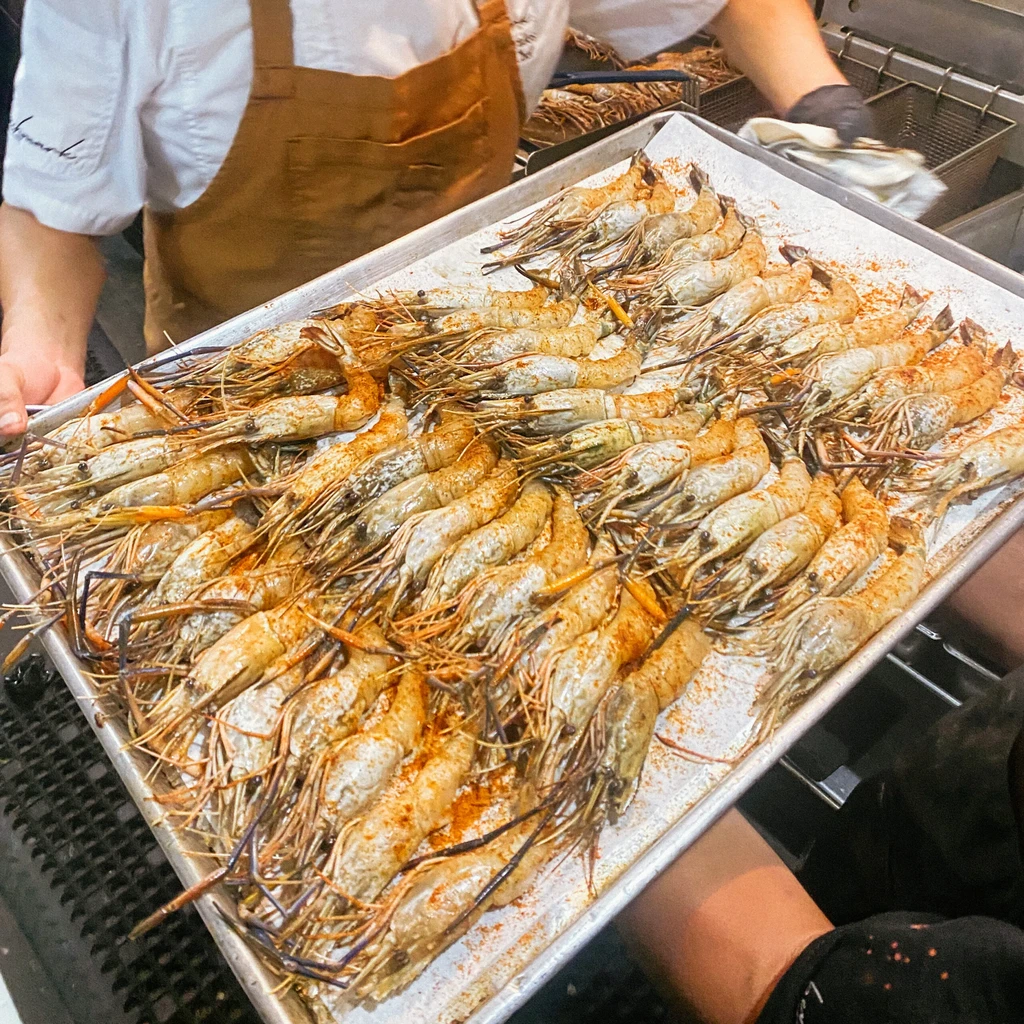 Tray of raw, spice-seasoned shrimp held by kitchen staff.
