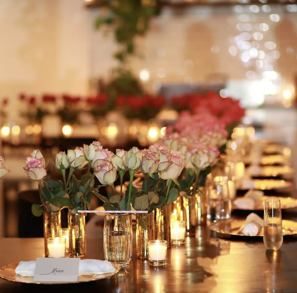 Elegant table set with roses, candles, golden plates, and name card.