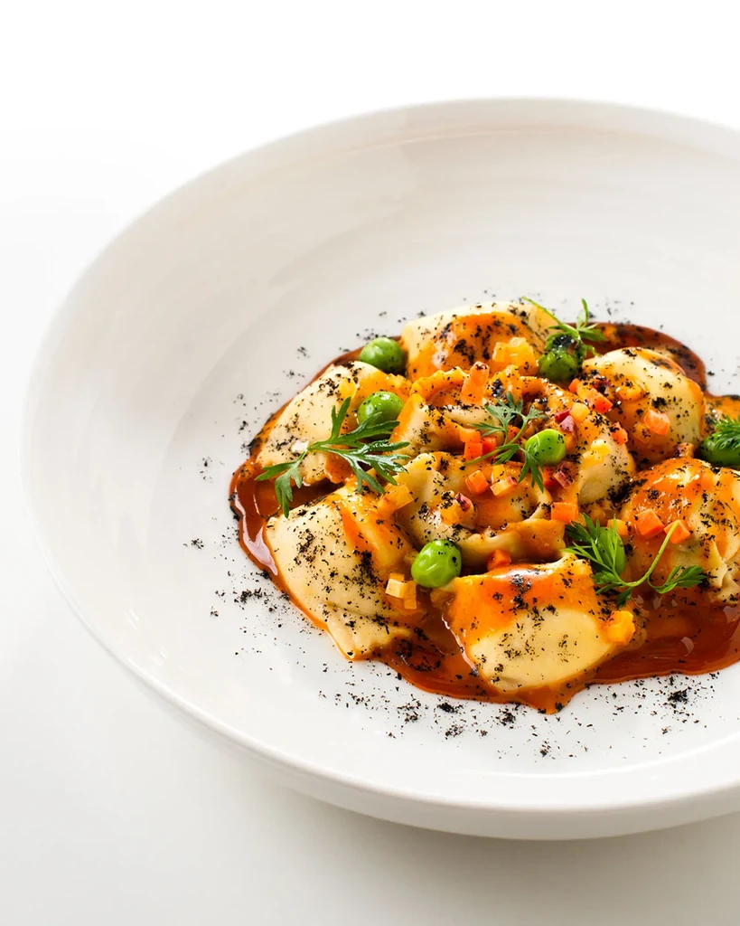 Pasta with orange-brown sauce, green peas, and fresh herbs.