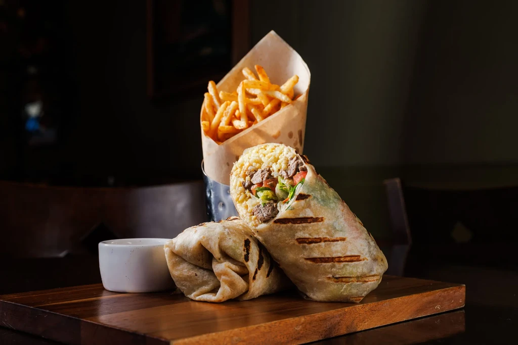 Two grilled burritos, one cut open, with fries and dipping sauce.