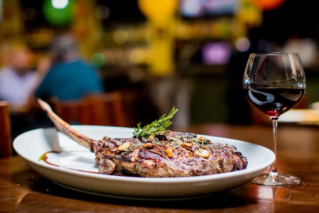 Tomahawk steak with rosemary, red wine, blurred restaurant background.