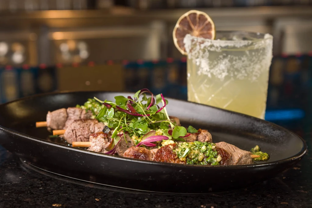 Close-up: Grilled meat skewers with garnish and a salted margarita.