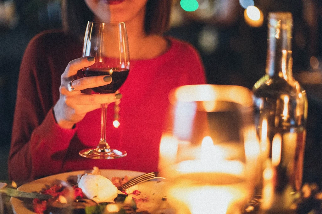 Hand with dark nails holds red wine in a warm, blurred setting.
