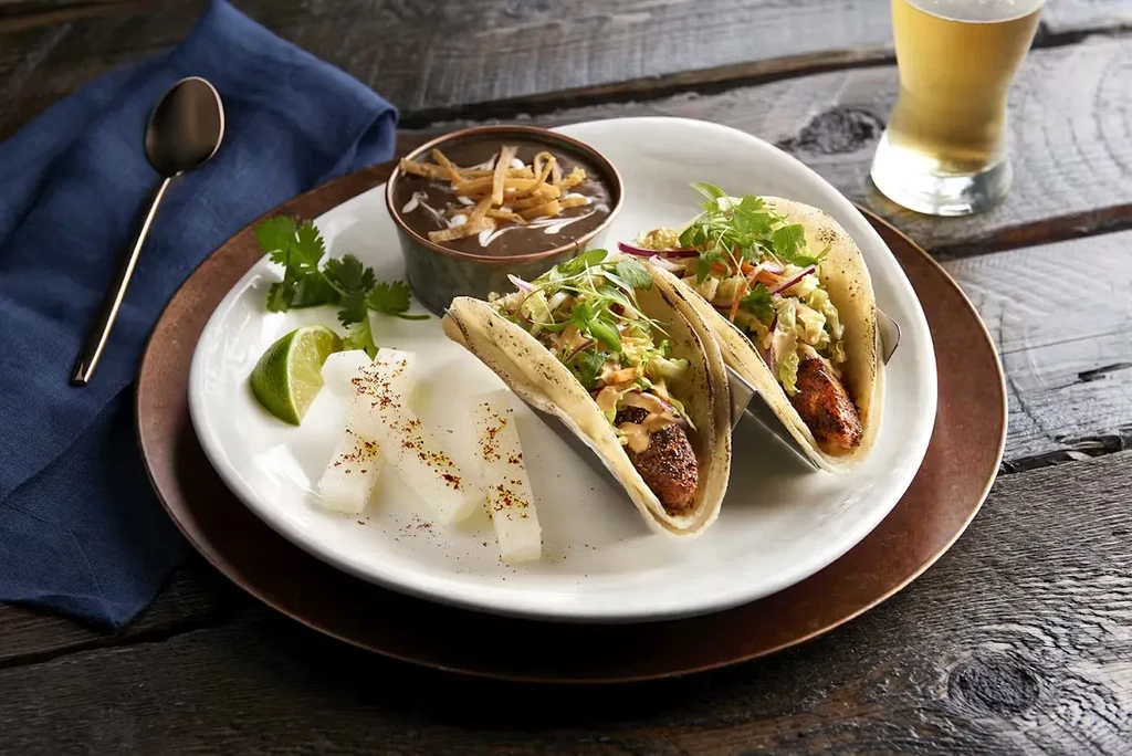 Two tacos, black bean soup, jicama, beer on a rustic table.
