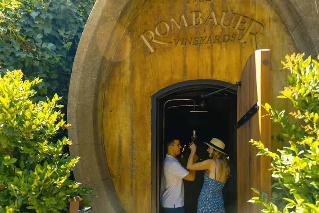 Two people toast inside Rombauer Vineyards' barrel-shaped wooden entrance.