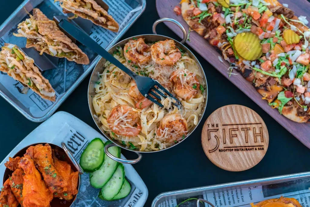 Flat-lay of pasta, tacos, pizza, wings from The 5ifth Restaurant.