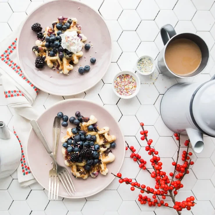 Overhead breakfast of berry waffles with sprinkles, whipped cream, and coffee.