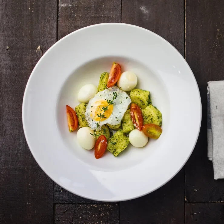 Overhead photo of gnocchi with pesto, sunny-side-up egg, tomatoes, mozzarella.