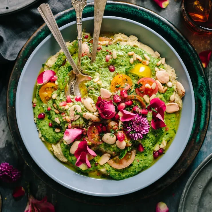 Top-down view of a vibrant green dip with colorful toppings and edible flowers.