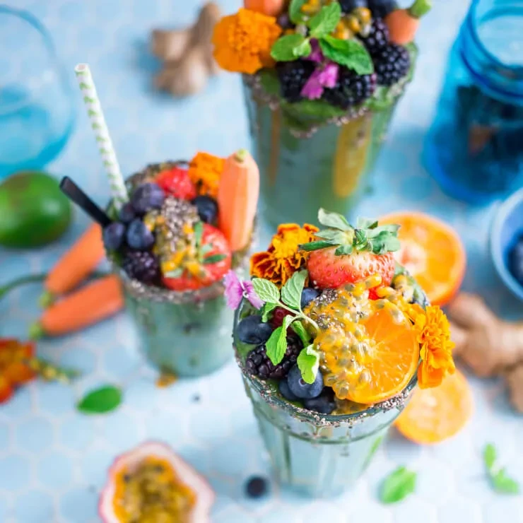 Three vibrant green smoothies garnished with fresh fruits, mint, and flowers.