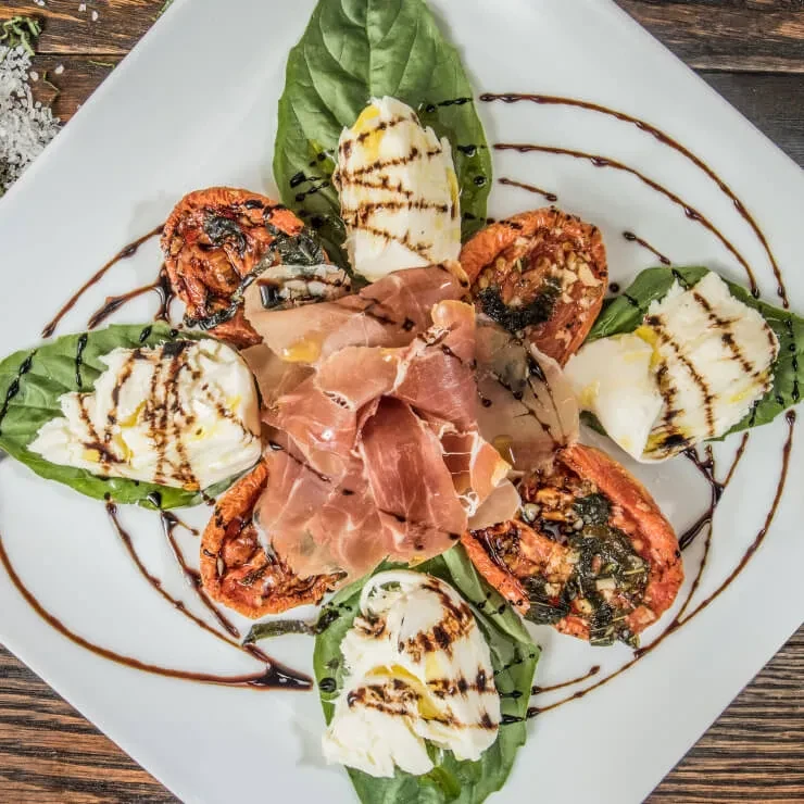 Appetizer plate with prosciutto, mozzarella, tomatoes, basil, and balsamic.