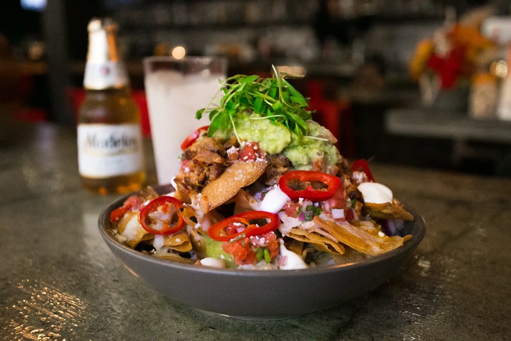 Dark bowl of nachos topped with meat, guacamole, pico, and beer.