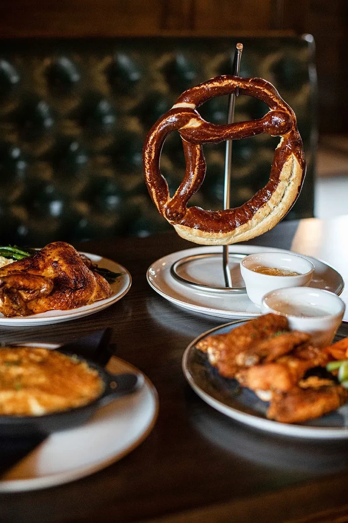 Close-up: pretzel on stand, roasted chicken, and various pub dishes.