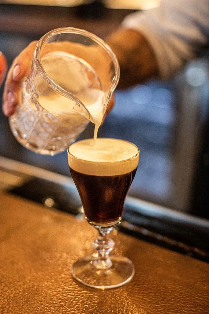 Close-up of hand pouring cream into a dark stemmed glass.