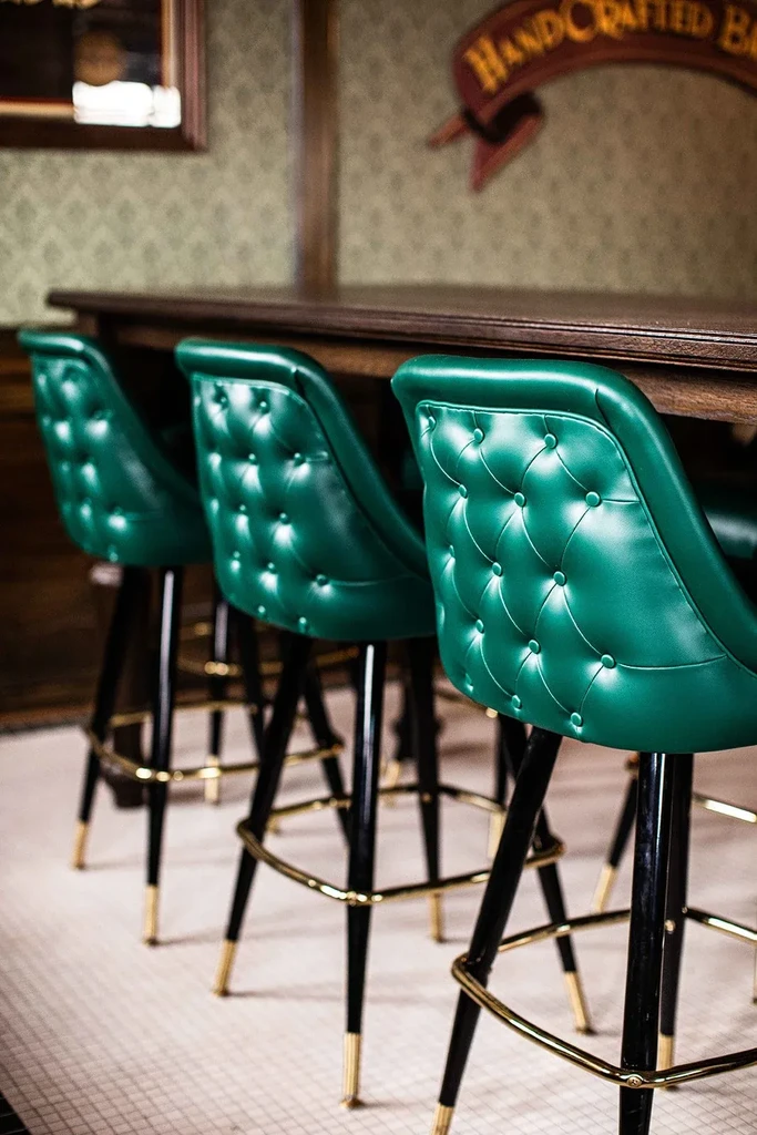 Three emerald green tufted bar stools at a dark wooden bar.