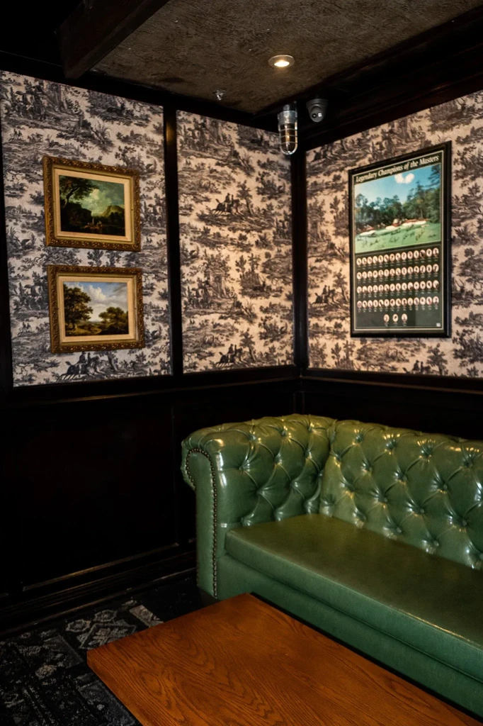 Green tufted sofa, wooden table, toile wallpaper, and Masters golf poster.