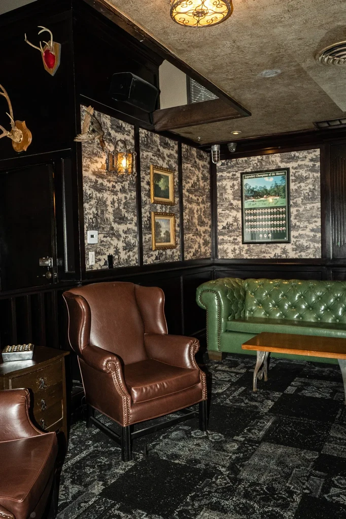 Classic, dimly lit lounge featuring leather furniture and detailed toile wallpaper.