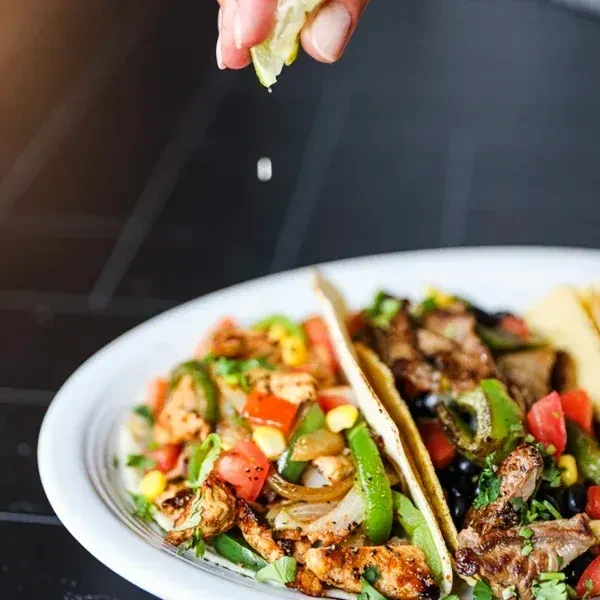 Two chicken and steak tacos, richly filled, hand squeezes lime.