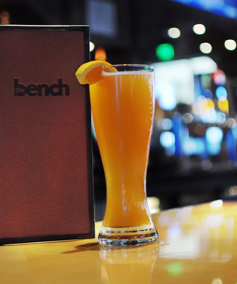 Frothy orange beverage with lemon wedge and "the bench" menu.