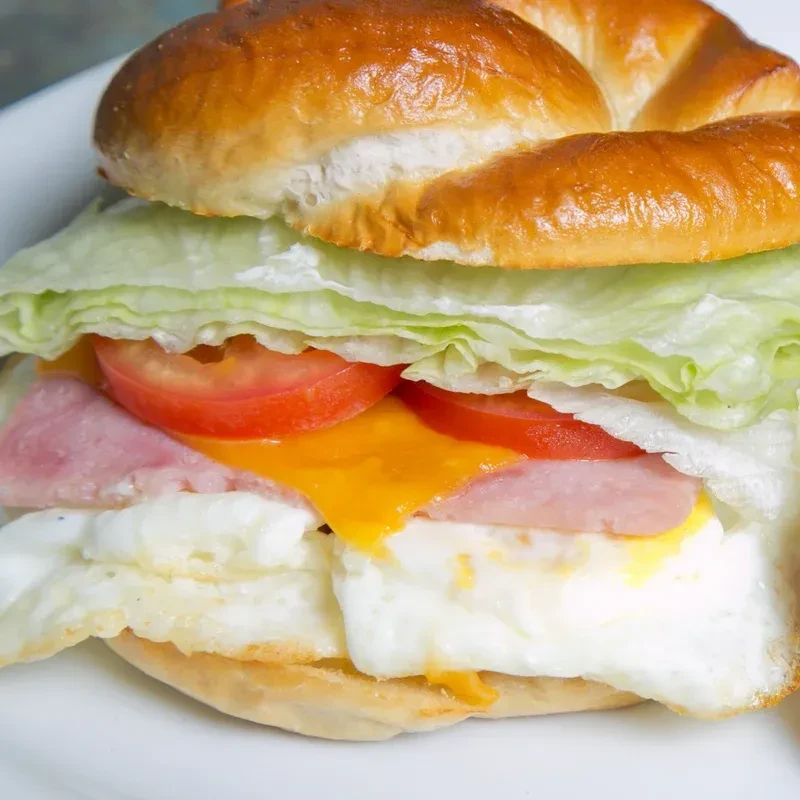 Layered breakfast sandwich with egg, melted cheese, ham, lettuce, tomato.