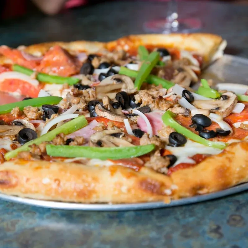 Generously topped baked pizza with pepperoni, sausage, vegetables, slice removed.