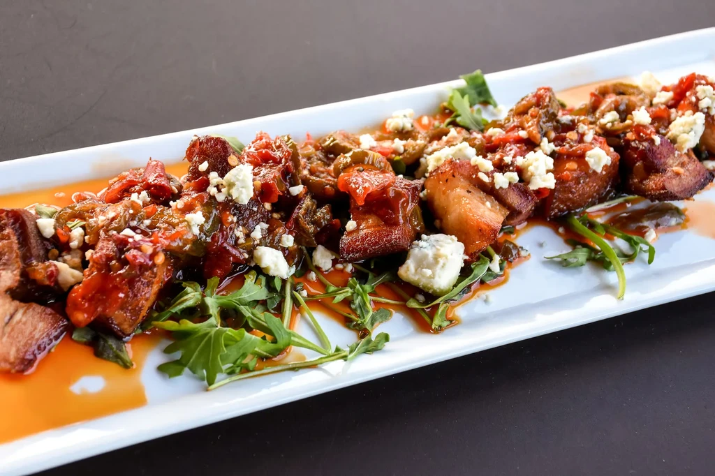 Browned pork belly in red sauce, garnished with arugula and cheese.
