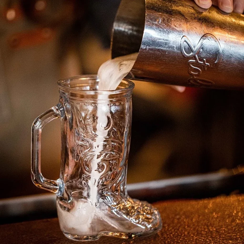 Frothy drink poured from shaker into intricate cowboy boot glass.