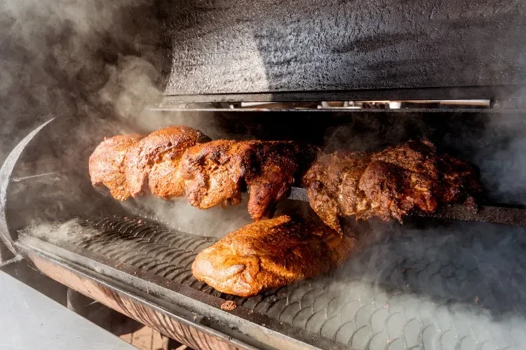 Browned, seasoned meat smoking inside a large industrial smoker.
